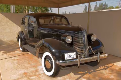Vintage black classic car parked under a covered outdoor area at a facility.