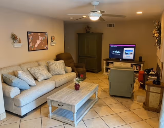 Cozy beige living room with sofa, TV, coffee table, and ceiling fan.