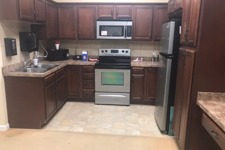A kitchen area with dark wooden cabinets, a stainless steel oven and microwave, a stainless steel refrigerator, a double sink, and a countertop with various small appliances and items.