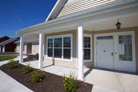 Front exterior of a cottage-style senior living entrance with porch pillars.