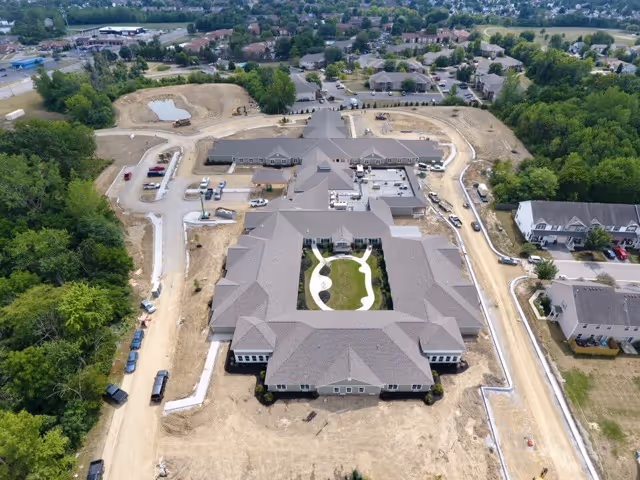 Aerial view of a large U-shaped senior living facility under construction with a central landscaped courtyard and surrounding roads.