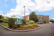 Exterior view of a multi-story senior care facility building with a landscaped entrance area featuring bushes, flowers, and a sign that reads 'East Care Center'. The sky is partly cloudy.