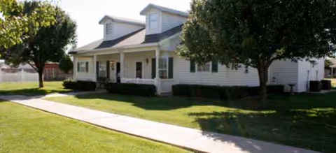 White, single-story senior living facility exterior with a manicured lawn and trees.