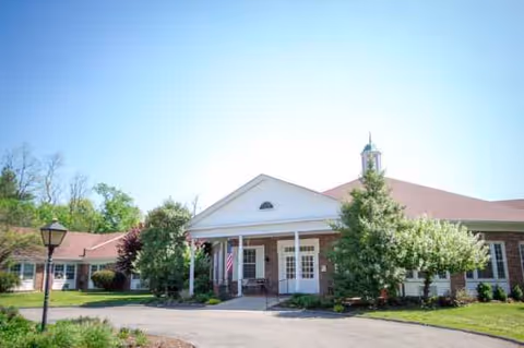 Front view of Mayfair Manor senior living facility with columns, flag, and landscaping.