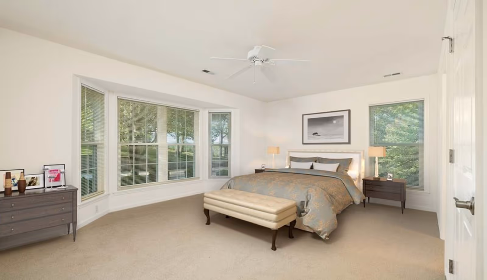Bright, spacious bedroom with a large bay window, king bed with bench at the foot, two nightstands, and a dresser.