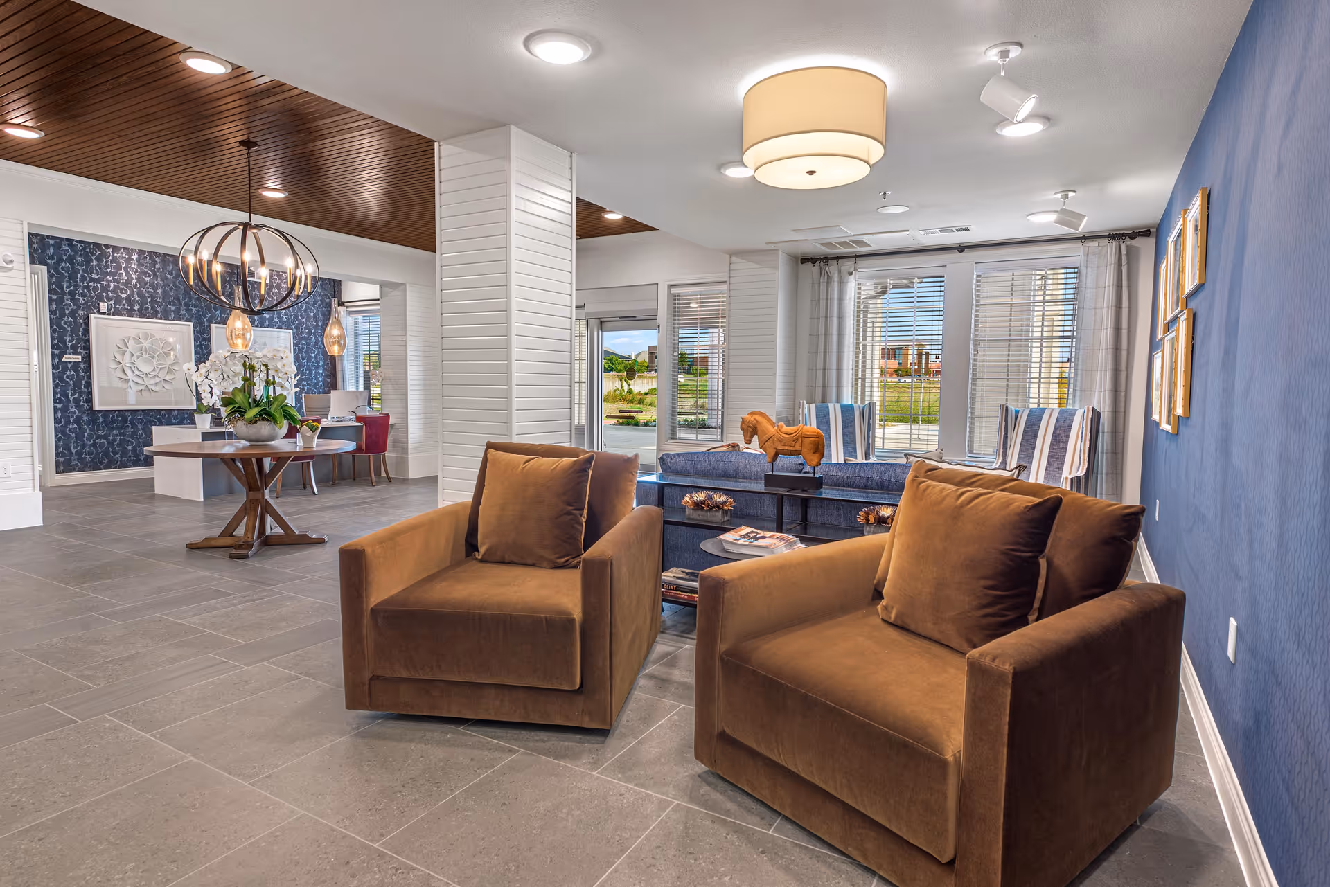 Modern lounge area with two brown armchairs facing a coffee table and blue seating, and a dining table visible in the background.