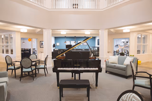 Spacious assisted-living common room with a grand piano centered among seating and dining areas.