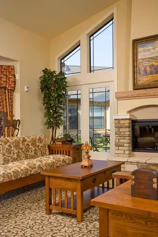 Sunlit living room with floral sofa, coffee tables, fireplace, and large windows.