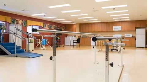 Bright rehab gym in a senior living facility with parallel bars and equipment.