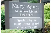 Outdoor sign for Mary Agnes Assistive Living Residence among shrubs stating it specializes in early dementia and Alzheimer's care.