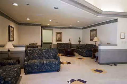 Interior senior living lounge with floral seating, lamps, and a tiled floor.