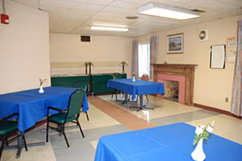 Dining room with blue tablecloths and green chairs in a senior facility.