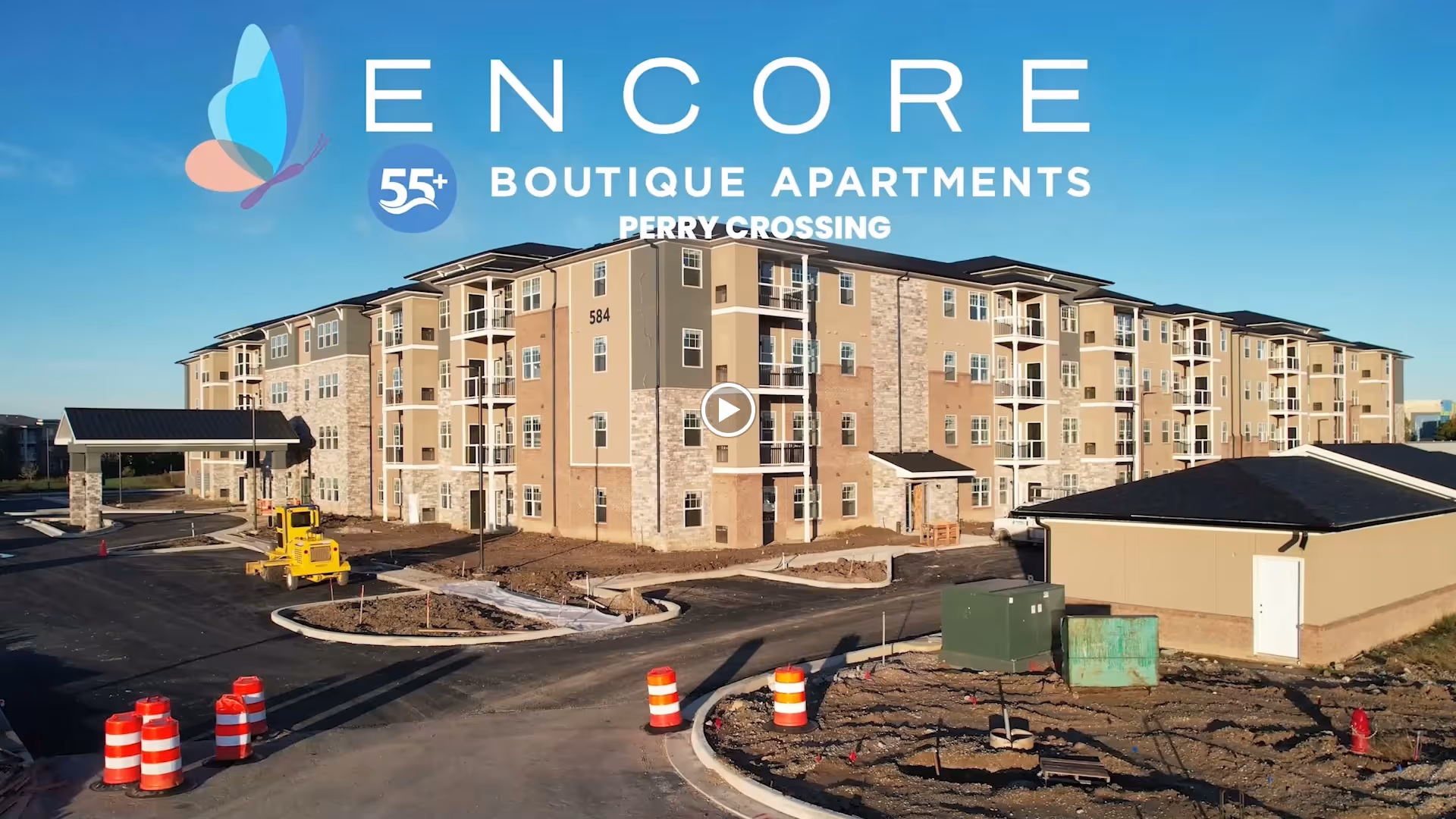 Exterior view of a multi-story Encore 55+ boutique apartment building with parking areas, construction equipment, and traffic barrels.