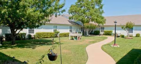 Brookdale Mansfield exterior with curved path, green lawn, and trees in front of a low-rise building.