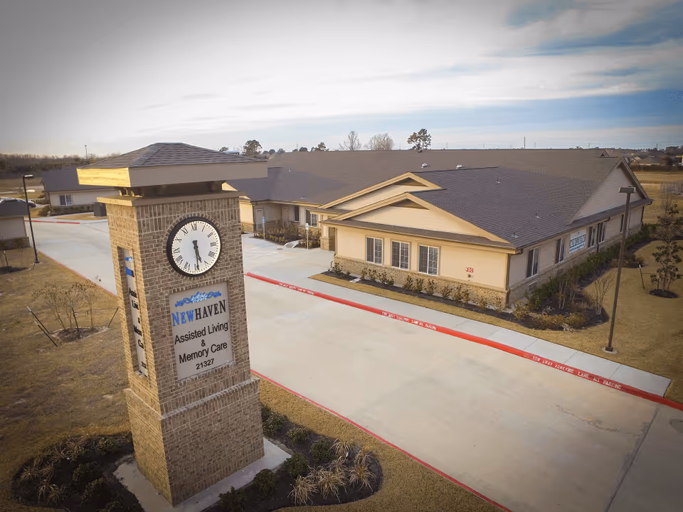 Aerial view of the NewHaven Assisted Living & Memory Care building with a brick clock tower sign at the driveway entrance.