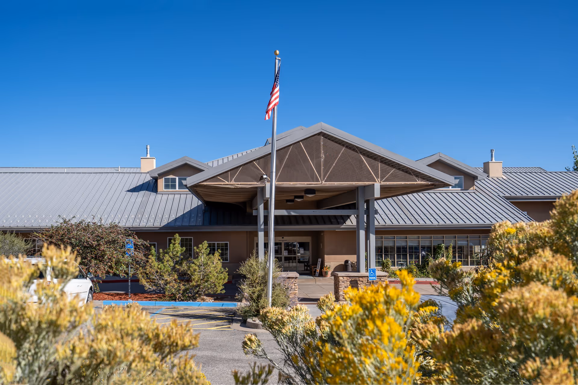 The entrance facade of the Los Alamos facility, featuring a peaked roof, large windows, and a flagpole, surrounded by greenery and shrubs.