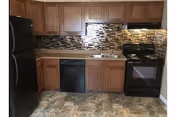 Kitchen area with wooden cabinets, a black refrigerator, black dishwasher, black stove with oven, and a tiled backsplash. The floor has a patterned tile design.