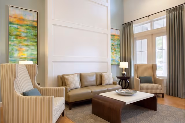 Bright, well-appointed living room with a sofa, two armchairs, a coffee table, lamps, large windows with curtains, and abstract wall art.