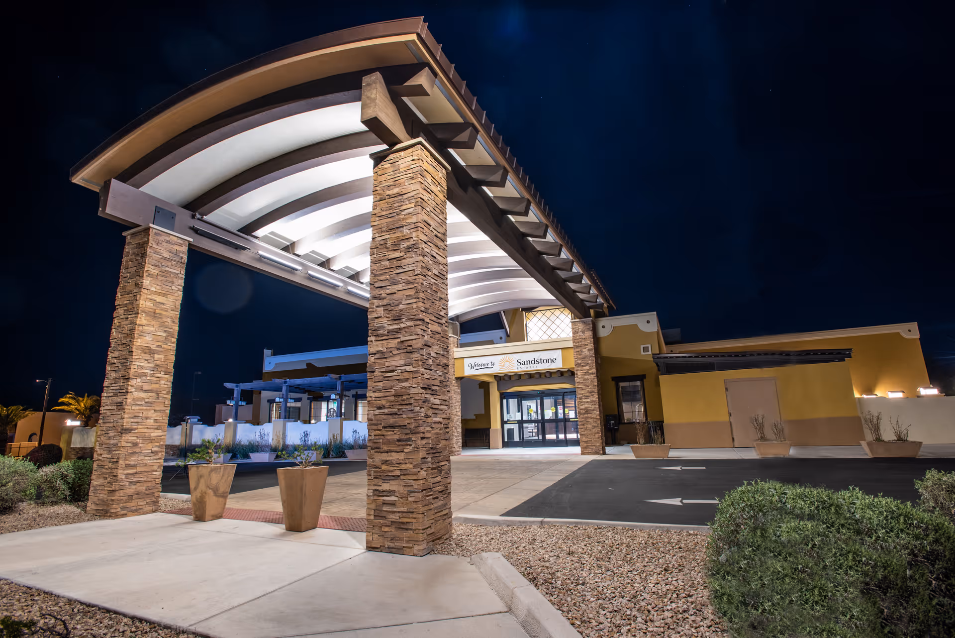 Nighttime view of the illuminated entrance canopy and front facade of the Sandstone Estates building.
