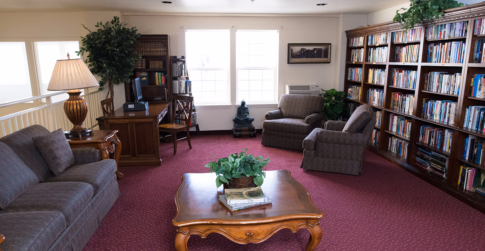A cozy interior lounge with tall bookshelves, upholstered chairs and a sofa arranged around a wooden coffee table.