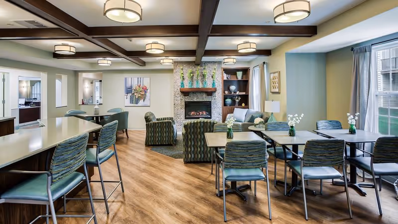 Bright communal dining and lounge area with multiple tables and chairs, a fireplace, and seating.