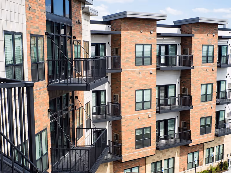 Exterior view of a multi-story brick senior living building with rows of balconies and windows.