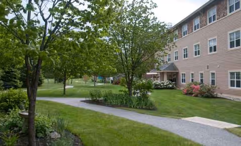 Exterior view of Bay Square at Yarmouth with lawn, trees, and walkway beside the building.