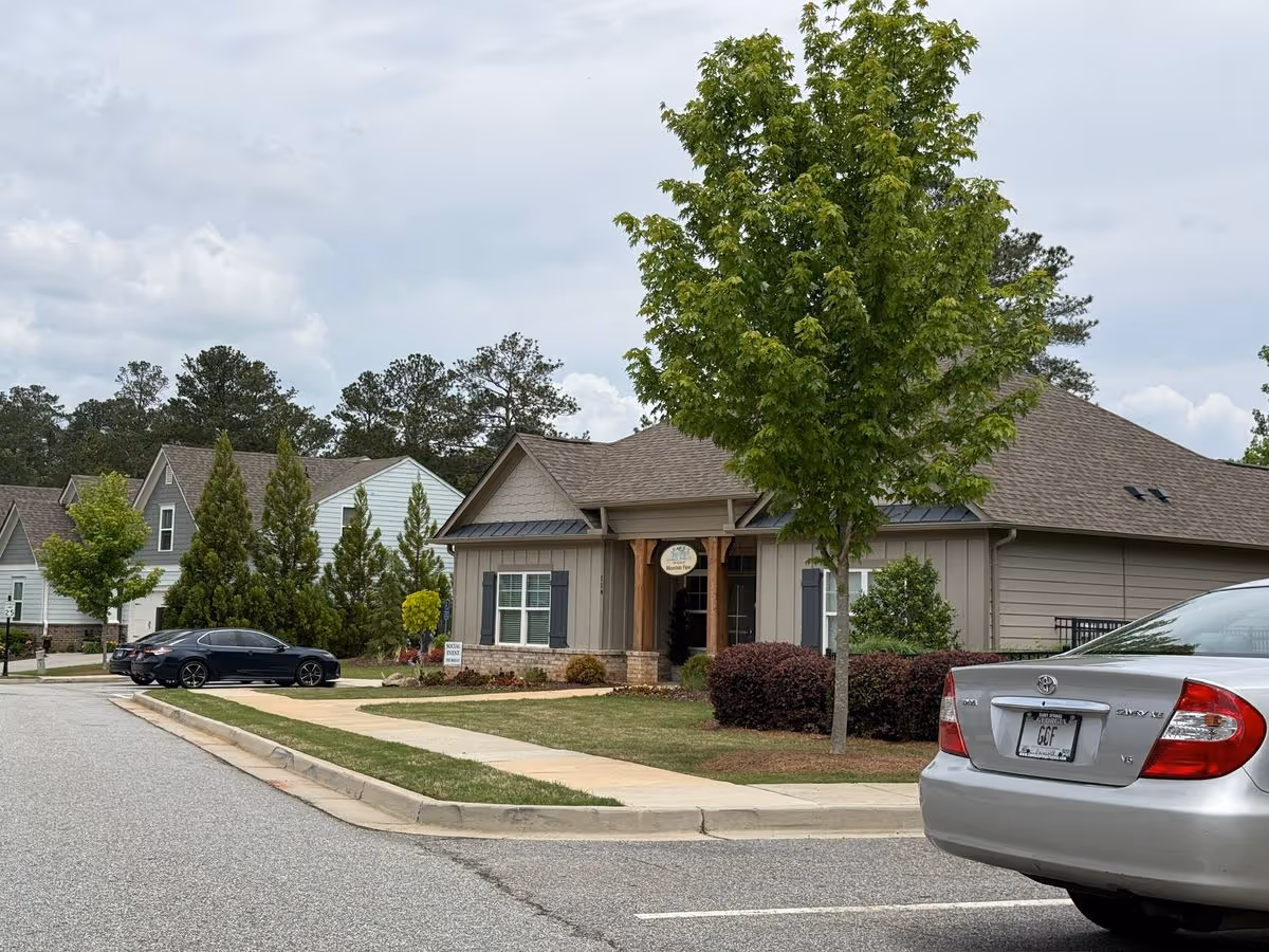 Front exterior of a single-story community building with a tree and parked cars along a residential street.