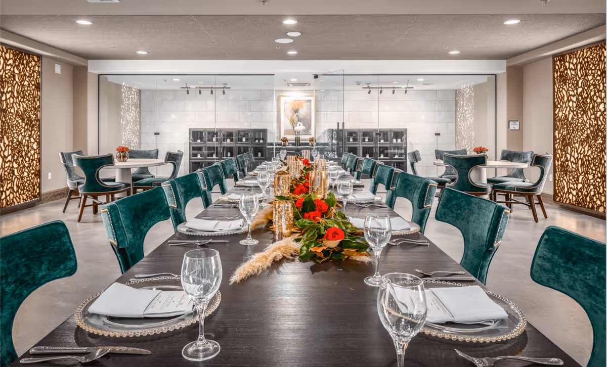 Long elegant dining table set for a meal with green upholstered chairs and a red floral centerpiece in a modern dining room.