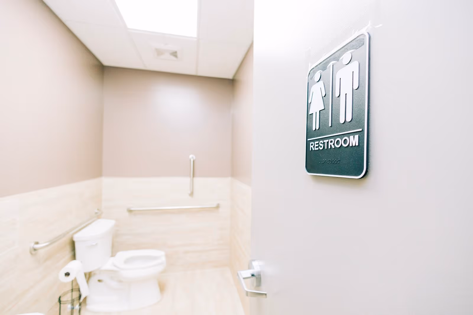View of a clean, accessible restroom with a white toilet, grab bars on the walls, and a restroom sign on the door showing male and female symbols.
