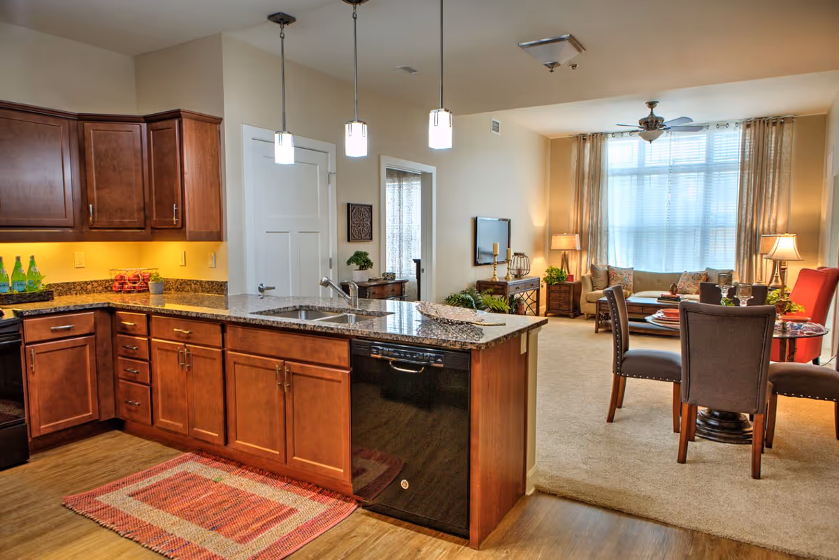 Open-plan kitchen with a granite island and dark wood cabinets opening into a furnished living and dining area.