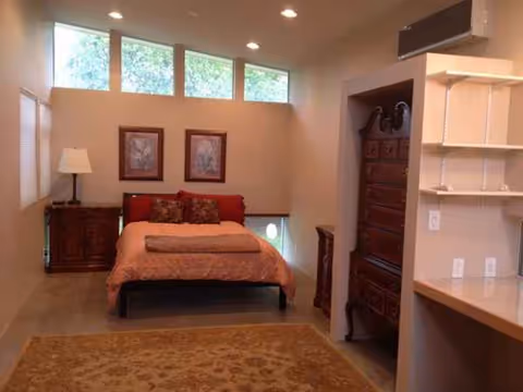 A cozy bedroom in a senior living facility with a bed, armoire, rug, and dresser.