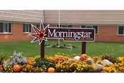 Sign reading "Morningstar Residential Care Center" in a landscaped flowerbed with pumpkins in front of a brick building.