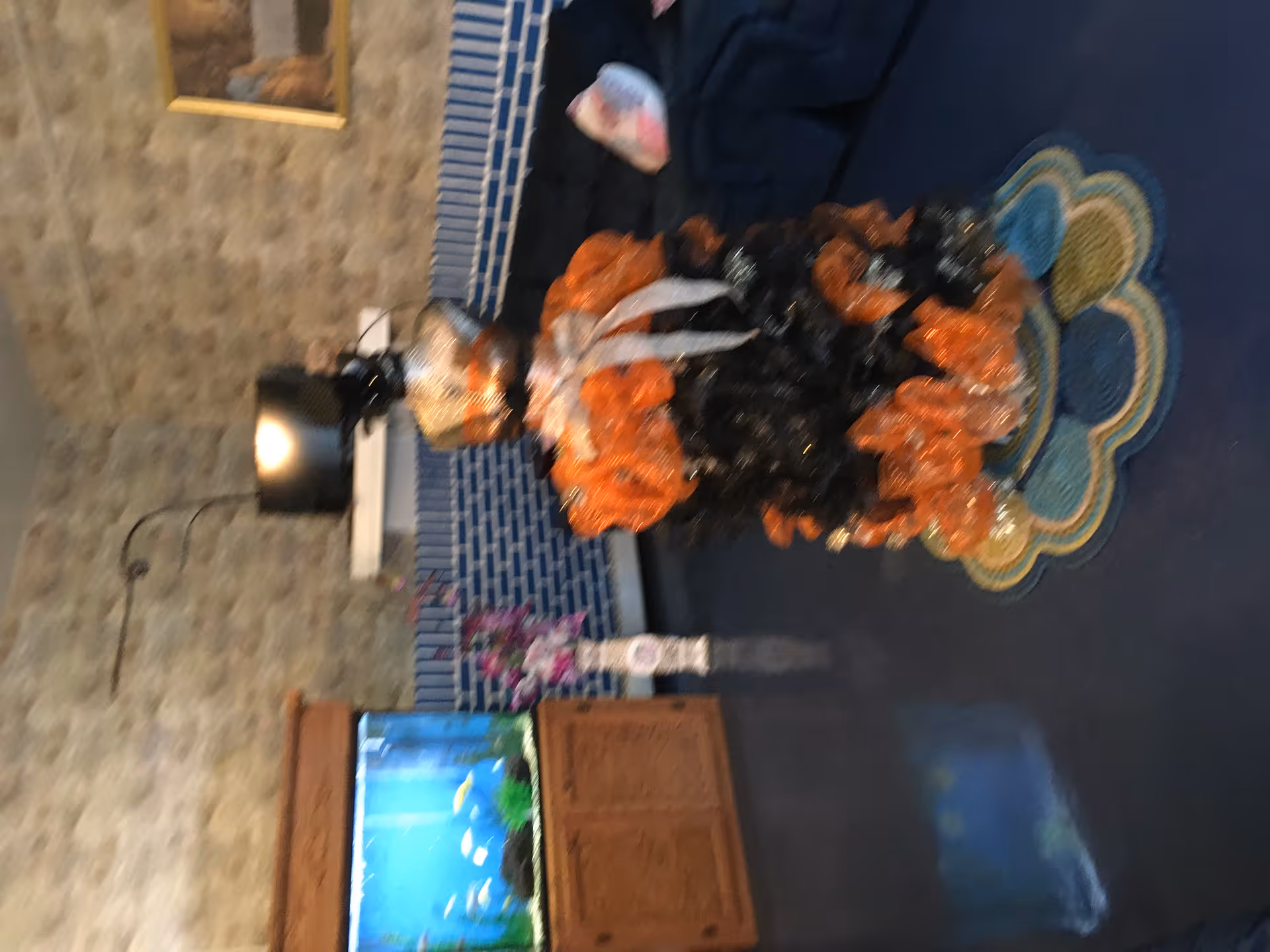 Interior common room with a decorative orange-and-black ribbon arrangement on a rug, an aquarium on a wooden cabinet, a lamp, and framed wall art.