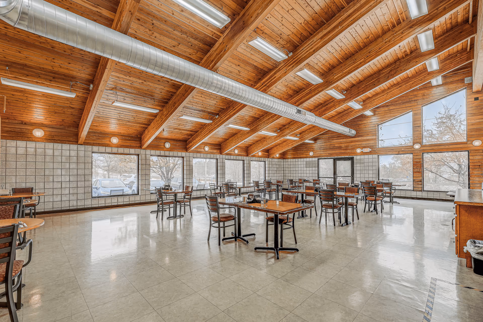 Spacious dining room with a vaulted wood ceiling, multiple tables and chairs, and large windows.