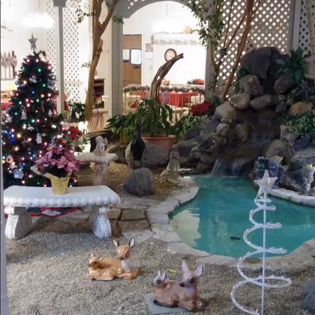 Indoor communal area with a small pond and waterfall, a decorated Christmas tree, benches, and decorative animal statues.