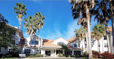 Sunlit exterior view of Venice Palms Senior Living building with palm trees.