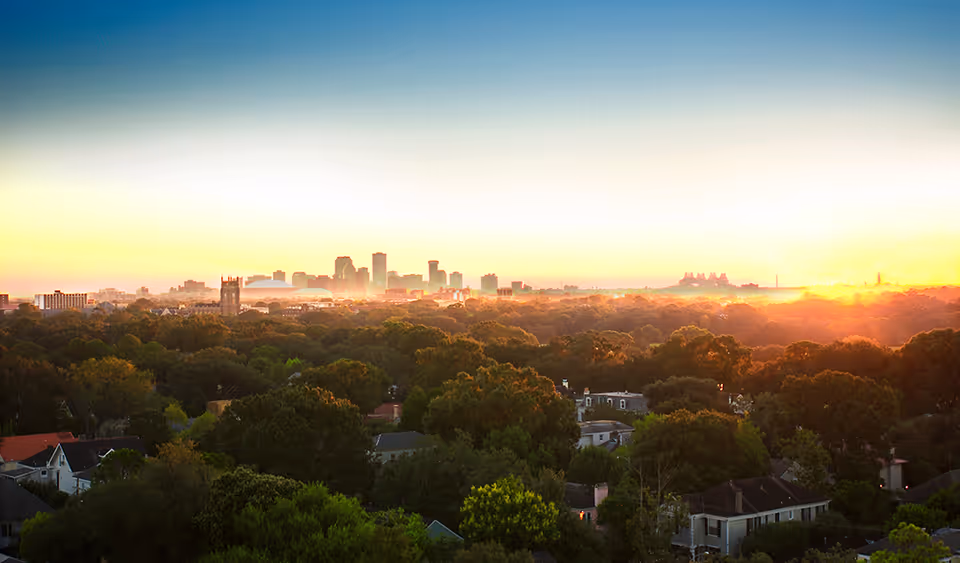 Panoramic view of a city skyline at sunrise above a tree-filled residential neighborhood.
