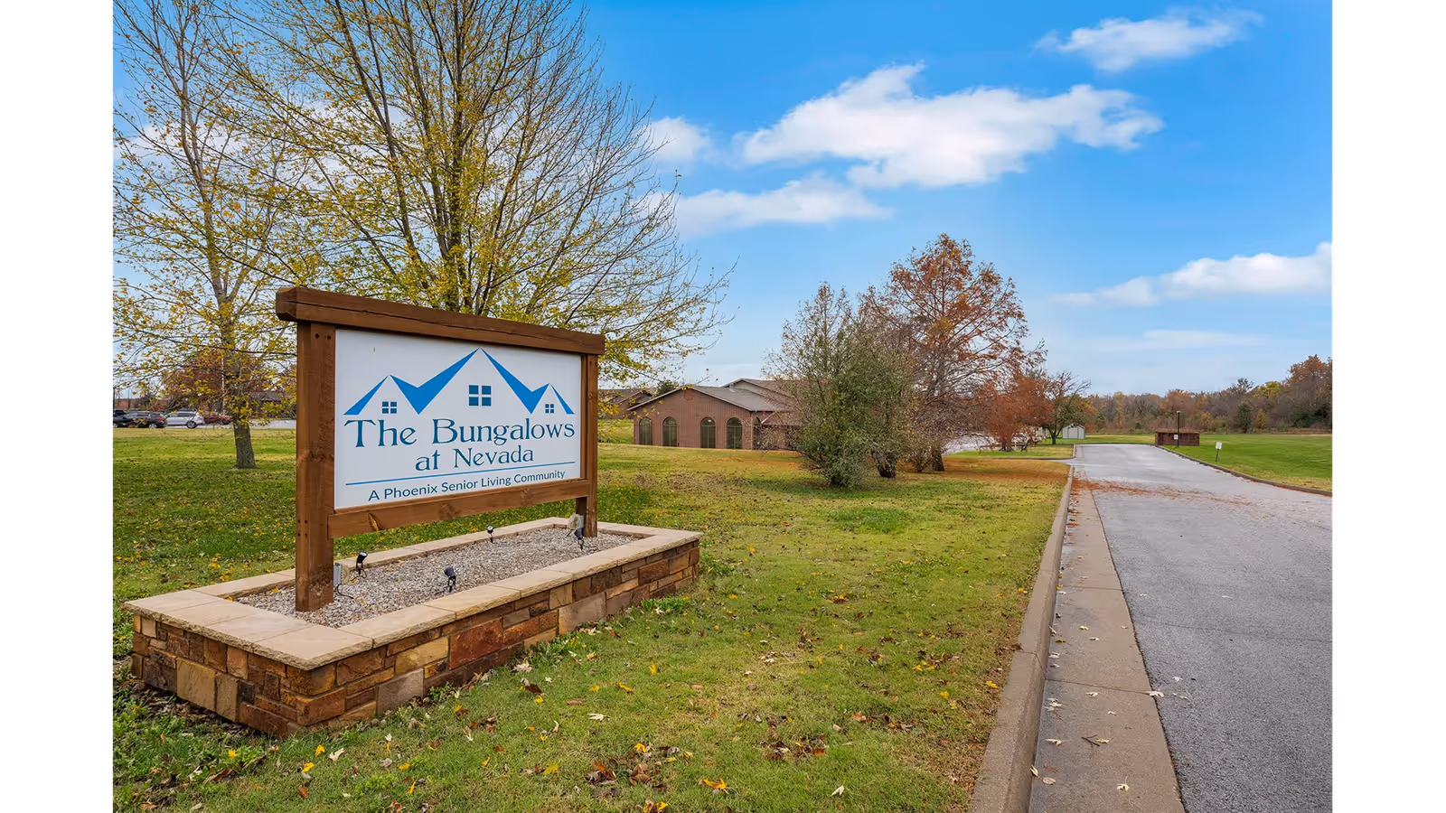 Outdoor view of The Bungalows at Nevada senior living community sign with a building and trees in the background under a partly cloudy blue sky.