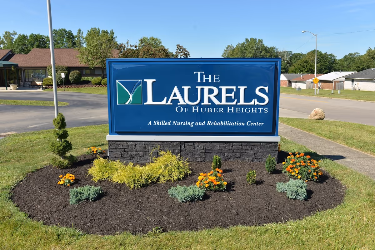Blue entrance sign reading 'The Laurels of Huber Heights' surrounded by landscaping in front of the facility.