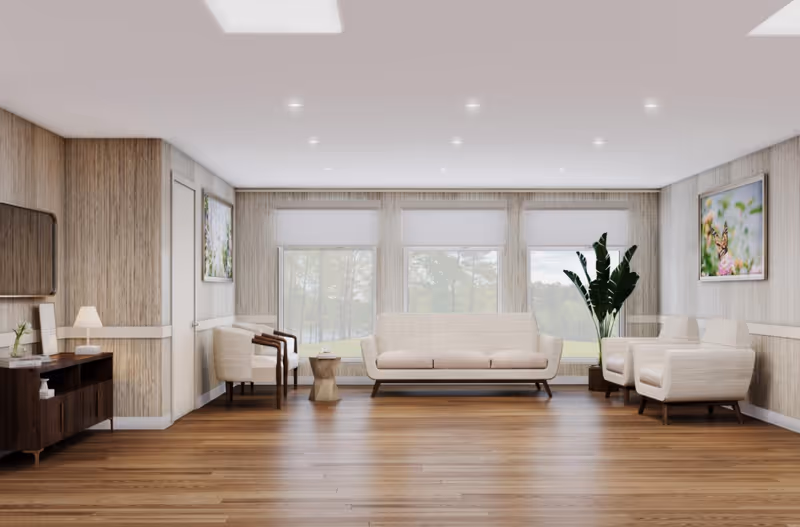 A bright and spacious living room with wooden flooring, beige upholstered sofa and armchairs, large windows with white blinds, a wooden sideboard with a lamp and decor, and framed nature artwork on the walls. A tall green plant is placed near the right corner.