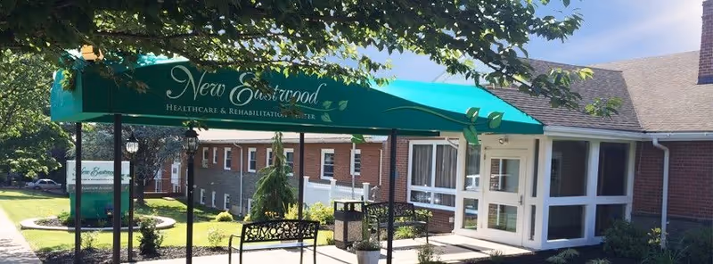 Entrance of New Eastwood Healthcare & Rehabilitation Center with a green awning, benches, and a brick building facade.