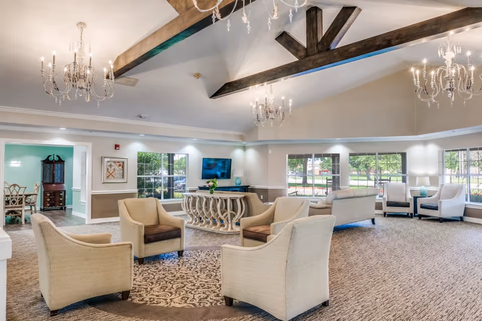Bright, spacious lounge with clustered armchairs and sofas, chandeliers, exposed ceiling beams, and large windows.