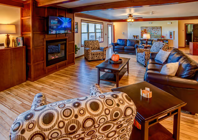 Spacious communal living room with leather sofas, patterned armchairs, a coffee table, hardwood floors, and a wall-mounted TV above a fireplace.
