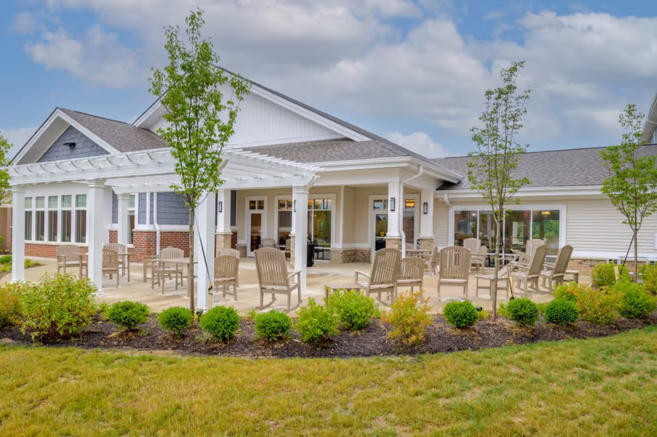 Outdoor patio area with multiple chairs and a pergola in front of a single-story senior living building.