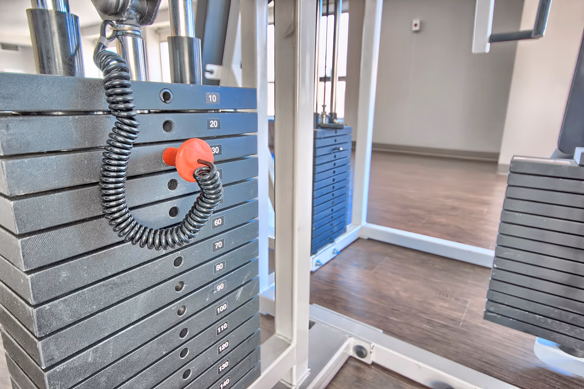 Close-up of a weight stack and red selector pin on a cable machine in a fitness room.