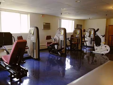 Fitness room inside a nursing facility with several exercise machines and a blue floor.