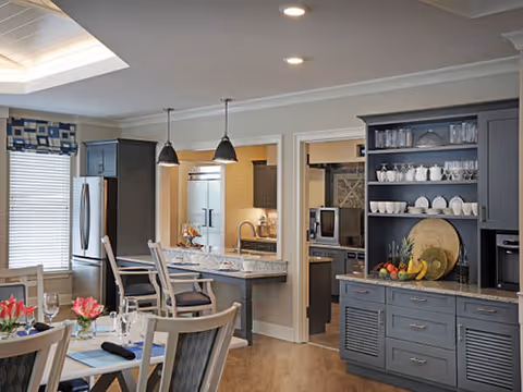 Open kitchen and dining area with gray cabinetry, a marble-topped island with pendant lights, stainless refrigerator, and a set dining table.