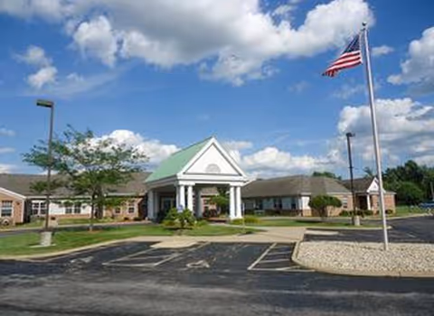 Orchard Grove facility exterior with a front entrance portico, parking, and American flag.