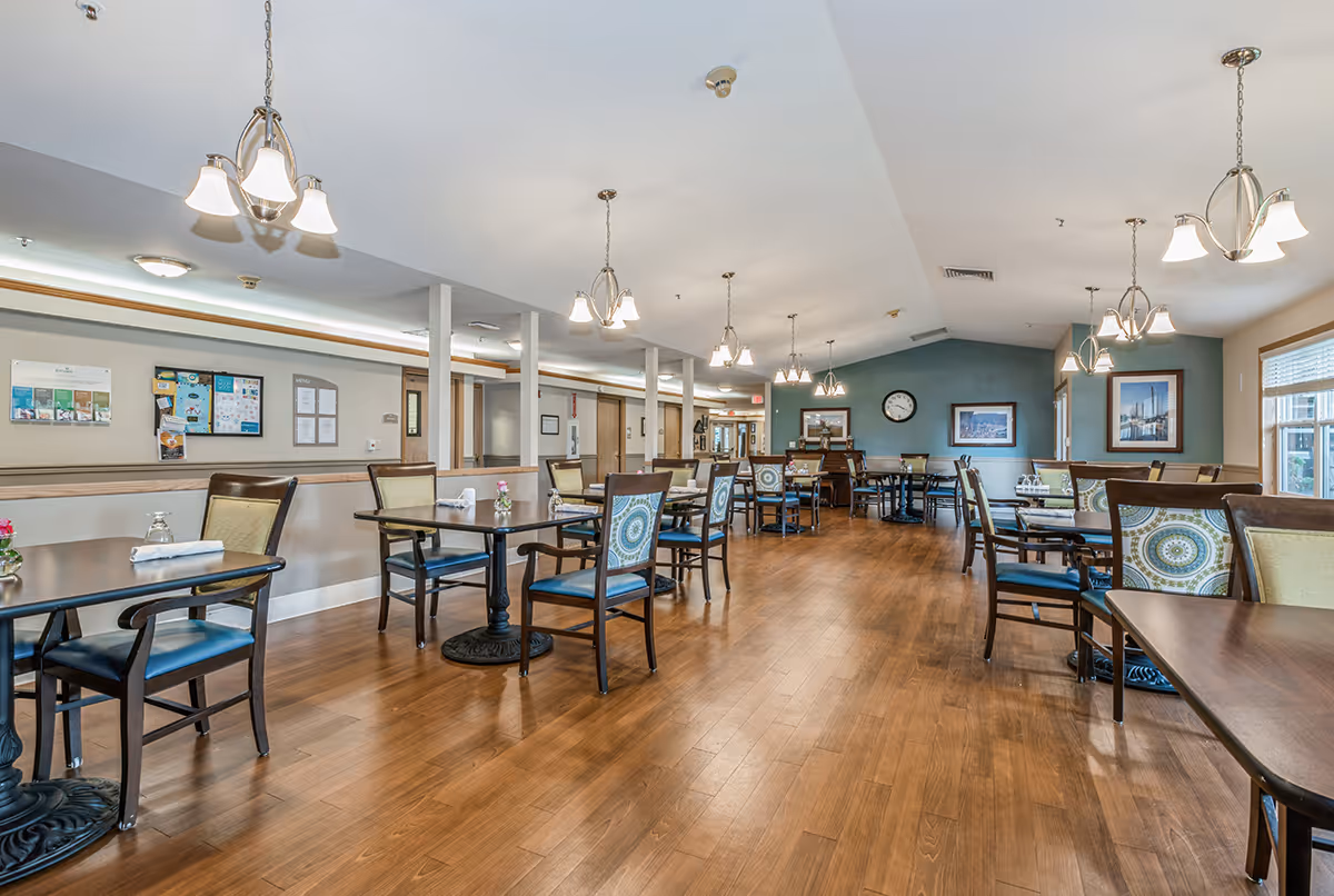 Spacious dining room with multiple tables and chairs, wood floors, pendant lighting, and framed artwork on the walls.